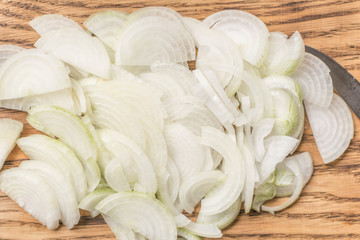 Sliced onions with half rings on a wooden chopping board on a wooden background.