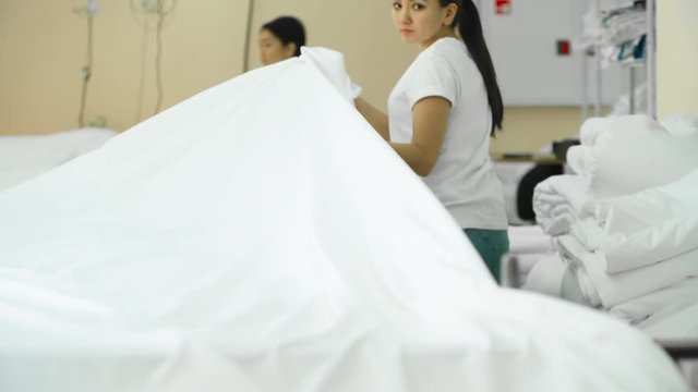 Tracking shot of female Asian factory workers pulling white cotton fabric on large table