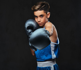 Portrait of a handsome young boxer in sportswear wearing gloves. Isolated on the dark background.
