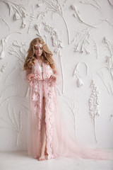 Delicate portrait of a young model girl. The image of the bride, a light lace dress in pink, a beautiful hairstyle and a natural make-up. Light photo studio, natural light from the window.