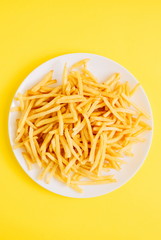French fries on yellow background. Potatoes fries in the on white plate. Flat lay, top view, copy space 