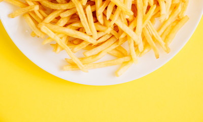 French fries on yellow background. Potatoes fries in the on white plate. Flat lay, top view, copy space 