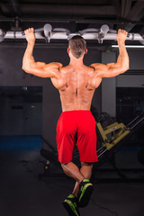 Fototapeta na wymiar Strong young man doing pull up exercise on horizontal bar in gym