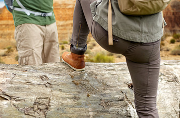 adventure, travel, tourism, hike and people concept - close up of woman with backpack climbing over fallen tree trunk over grand canyon national park background