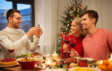 holidays and celebration concept - happy friends photographing at christmas dinner