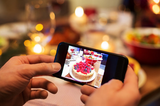 food, technology and holidays concept - close up of male hands photographing cake by smartphone at christmas dinner