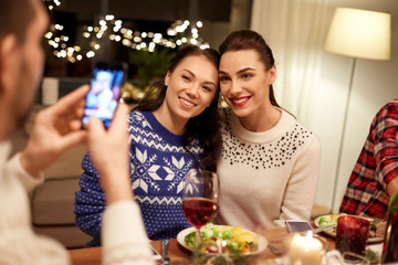 holidays and celebration concept - happy friends having christmas dinner at home and taking picture by smartphone