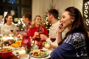 holidays, communication and celebration concept - happy young woman calling on smartphone and having christmas dinner with friends at home