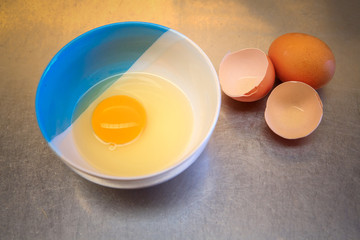 Cracked eggs in bowl and egg shells on stainless steel table.