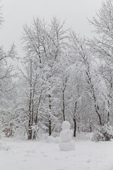Snowman and snow covered trees landscape. Snowfall in the park, winter weather scene. Gray day sky