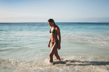 Young tanned woman sports figure walking along ocean coast sunset