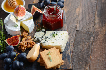 Cheese plate with grapes, figs, crackers, honey, plum jelly, thyme and nuts, selective focus.