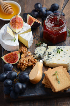 Cheese plate with grapes, figs, crackers, honey, plum jelly, thyme and nuts, selective focus.