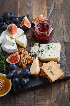 Cheese plate with grapes, figs, crackers, honey, plum jelly, thyme and nuts, selective focus.