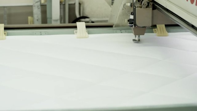 Close-up view of industrial textile machine quilting white fabric at factory