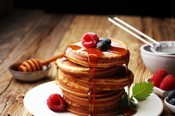 Pancakes with berries and maple syrup on rustic table