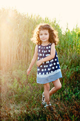 Naklejka na ściany i meble Little beautiful girl jumping and dancing in the rays of the setting sun