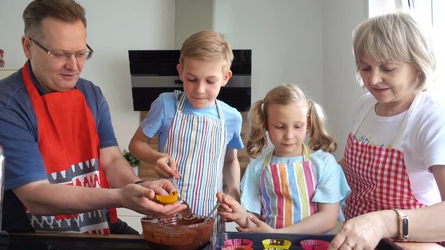 Happy grandparents have fun with their grandchildren preparing chocolate muffins in kitchen