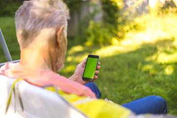 back view of senior retired man browsing the internet with phone with a green screen