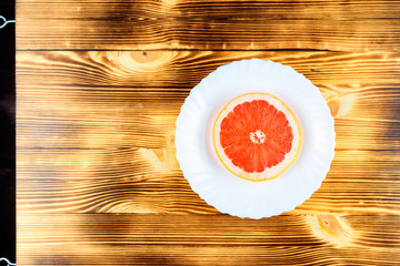 A fresh grapefruit on a white plate on a wooden background