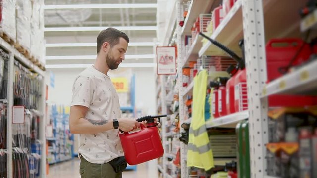 Grown brunet man holding a red canister for fuel in the hardware store, car products. Big red canister with a tube. Male customer.