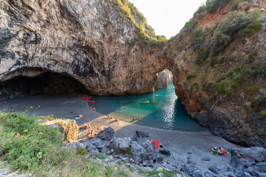 bathers in Arcomagno with a ray of sun at sunset (Arco magno), natural arch in San Nicola Arcella, Calabria, Italy