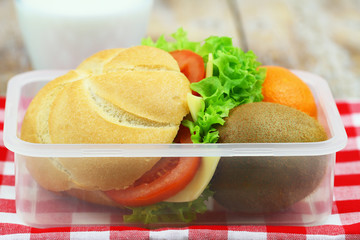 Healthy school lunch in transparent box containing cheese roll, kiwi fruit and mandarine
