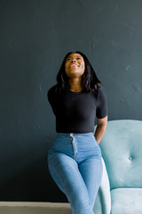 Close up shot of pleasant looking African American female has delighted look, healthy dark skin, poses indoor on sofa, has happy expression, expresses positive emotions. Facial expressions concept