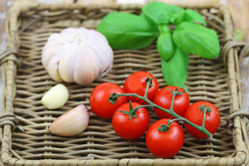 Organic ingredients: cherry tomatoes, basilicum leaves and garlic on wicker tray
