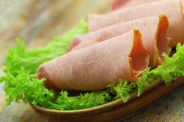 Slices of tasty ham on fresh lettuce leaves, closeup
