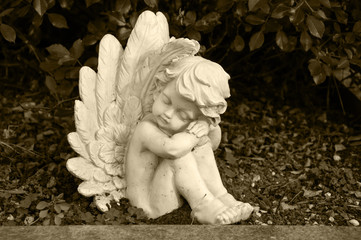 angel made of clay sitting in a hedge on a grave - sepia colored