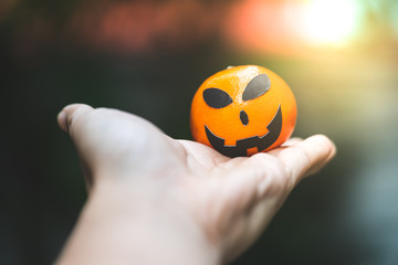 an oranges pumpkin face painting with scary on halloween party day on hand with blur background.