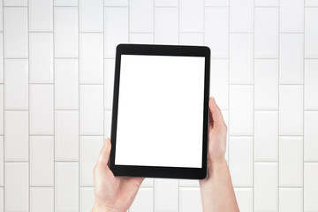 Hands holding tablet and brick tiles stacked in the background. Internal room such as a hospital, spa, bathroom, butcher's shop or toilet. Isolated screen with copy space.