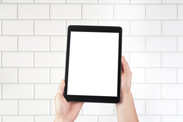 Hands holding tablet and brick tiles stacked in the background. Internal room such as a hospital, spa, bathroom, butcher's shop or toilet. Isolated screen with copy space.