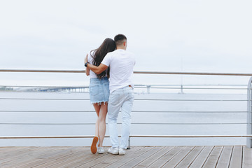 Young loving couple stands with their backs on sea promenade