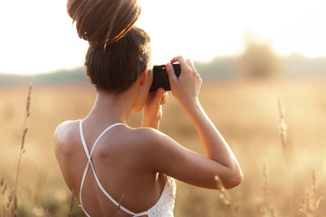 Young attractive girl with camera in field at sunset