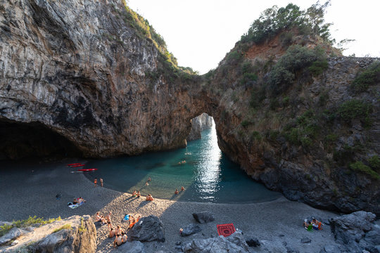 bathers in Arcomagno with a ray of sun at sunset (Arco magno), natural arch in San Nicola Arcella, Calabria, Italy