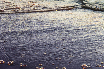 Waves on the sandy shore of a large river. The rays of light are reflected in the waves.