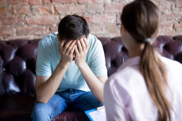 Young male visits psychologist counselor. Unhappy client covered face with hands, crying, feeling...