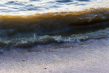Waves on the sandy shore of a large river. The rays of light are reflected in the waves.