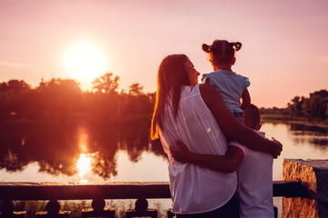 Happy family spending time outdoors hugging and enjoying the view of river at sunset. Mother with...