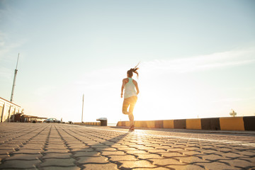 Side view of fitness woman running on a road by the sea. Sportswoman training on seaside promenade at sunset. © opolja