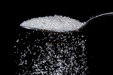 Pile of sugar in a teaspoon on a dark background. Sugar pouring from