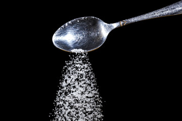 Pile of sugar in a teaspoon on a dark background. Sugar pouring from the top
