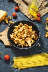 Uncooked pasta and chanterelle mushroom on dark stone background.