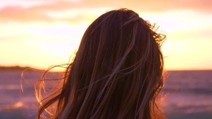 SLOW MOTION, CLOSE UP, LENS FLARE: Unrecognizable female photographer with wind in her hair looks at spectacular sunset over the ocean. Cool shot of woman looking for inspiration for her photography.