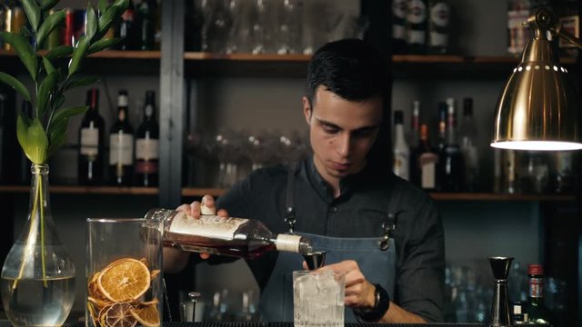 Close up shot of bartender hands preparing negroni cocktail with grapefruit. He is putting grapefruit skin into the cocktail glass on counter.