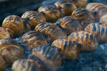 Baked potato with lamb fat on skewer over coals