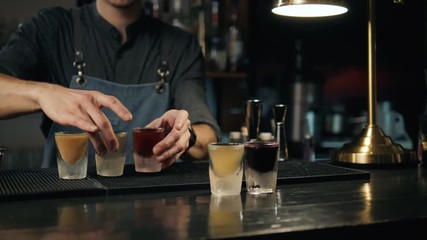 Beautiful row line of different colored alcohol cocktails bartender on a party, martini, vodka, and others on decorated catering bouquet table on open air event