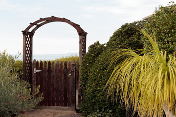 Natural wood picket gate opens to distant view of opportunity or mystery, surrounded by green...